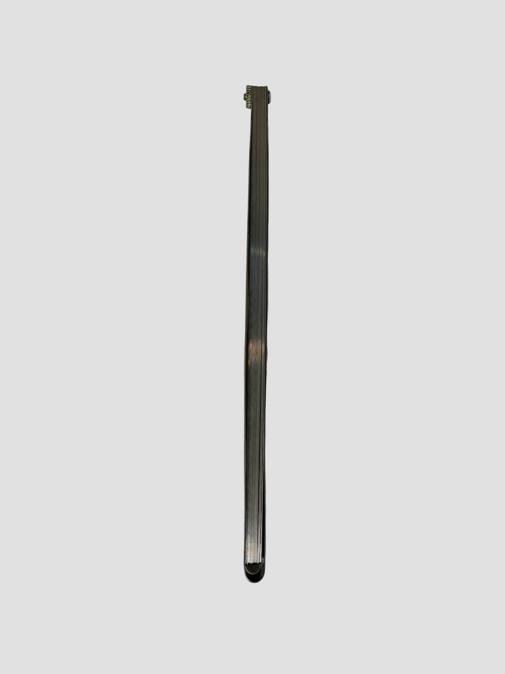 A long, narrow metallic silver component, possibly a metal strip or bracket, standing vertically on a light gray surface.