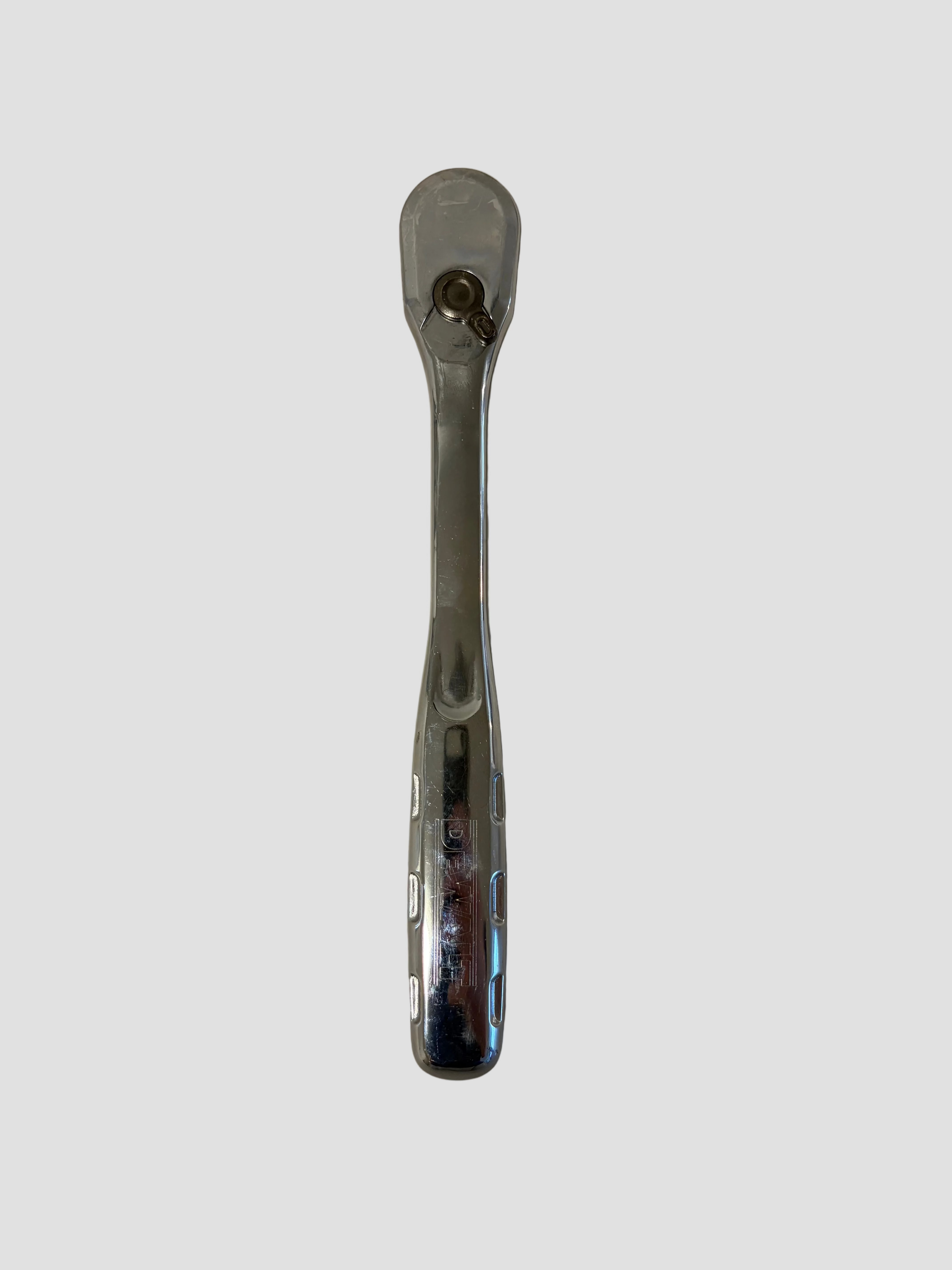 A chrome-finished ratchet wrench lying flat on a light-colored surface. The tool has a smooth, reflective handle with indented grip sections and a circular ratcheting head featuring a small directional lever and square drive socket connector. The lighting highlights the metallic sheen and slight wear marks on the handle.