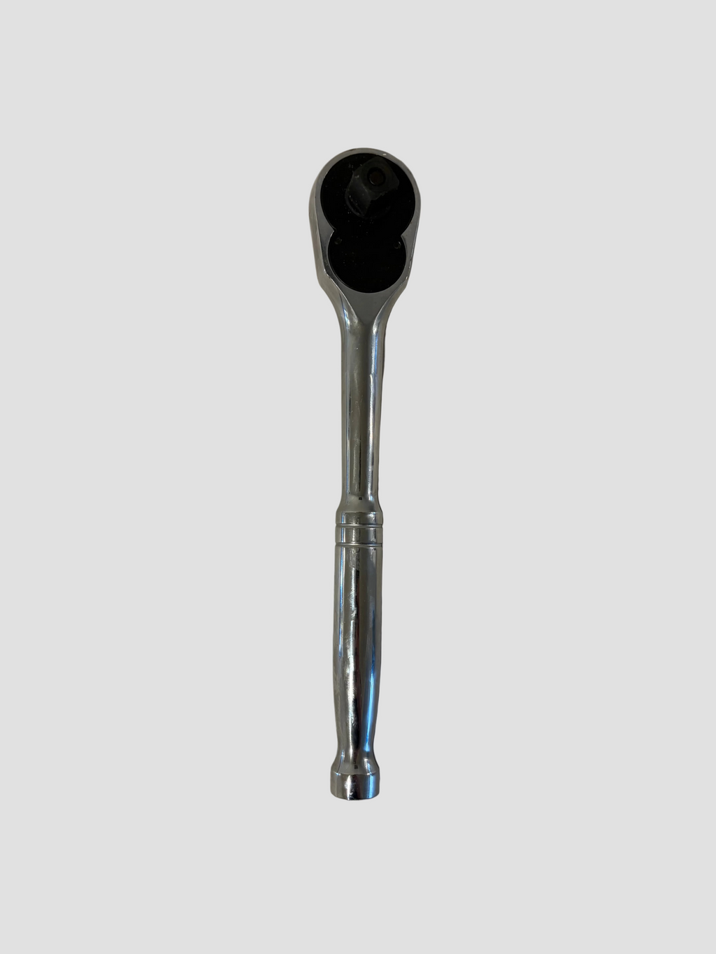 A chrome ratchet wrench with a black socket head, photographed vertically on a plain off-white surface.