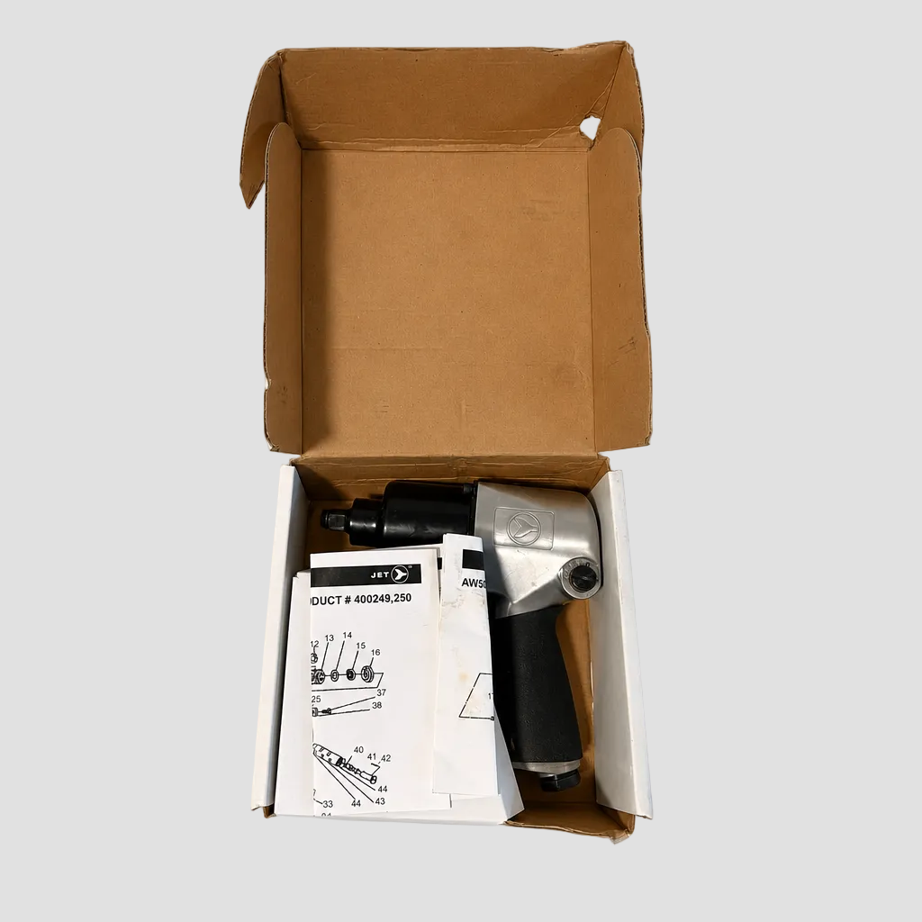 An open cardboard box containing a silver and black pneumatic air hammer tool with white instruction manuals, photographed from a top-down perspective on a light gray background.
