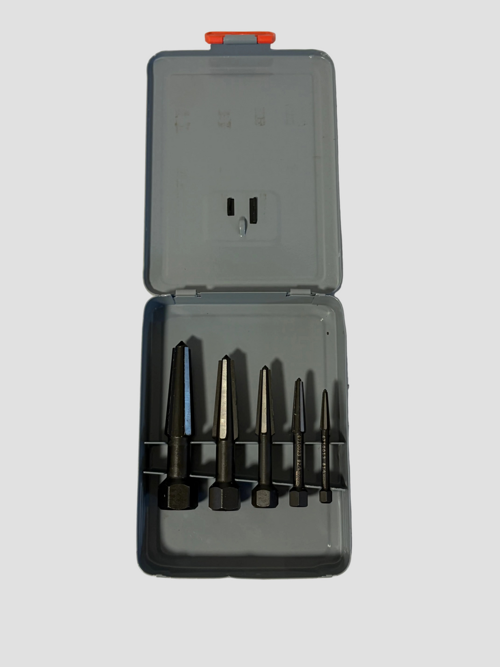 A set of four dark metal drill bits organized in a gray plastic case with a small orange-red latch on the lid, photographed on a light off-white surface.