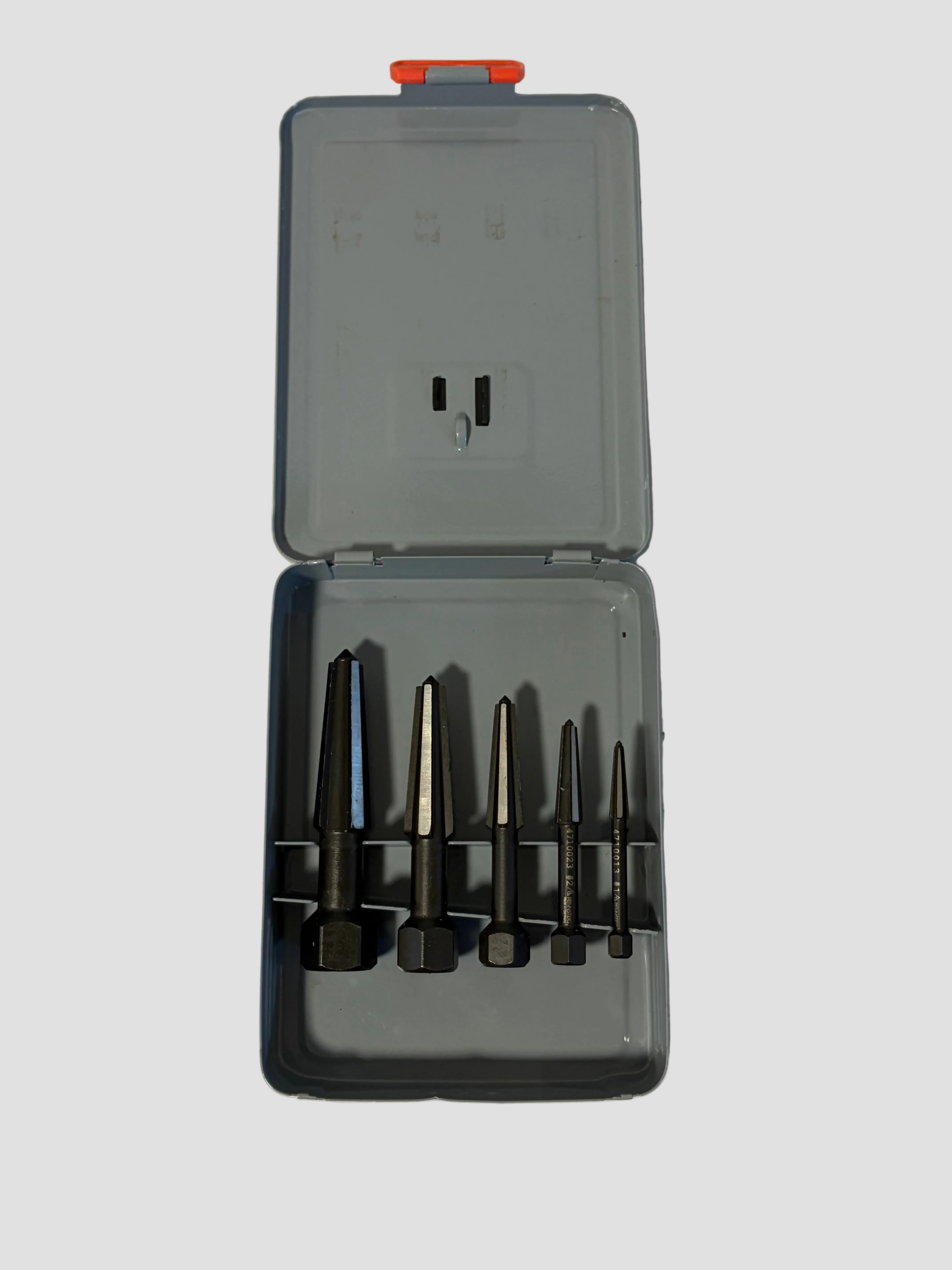 A set of four dark metal drill bits organized in a gray plastic case with a small orange-red latch on the lid, photographed on a light off-white surface.