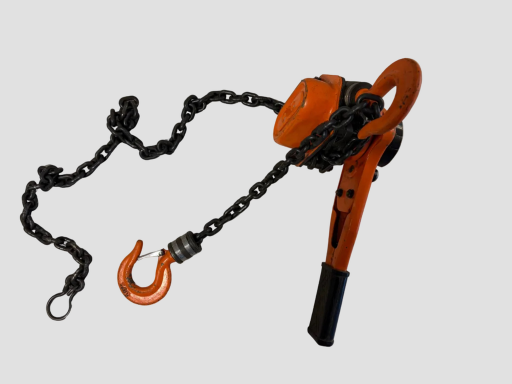 An orange and black hand chain hoist with a black metal chain and hook, photographed on a plain off-white surface.