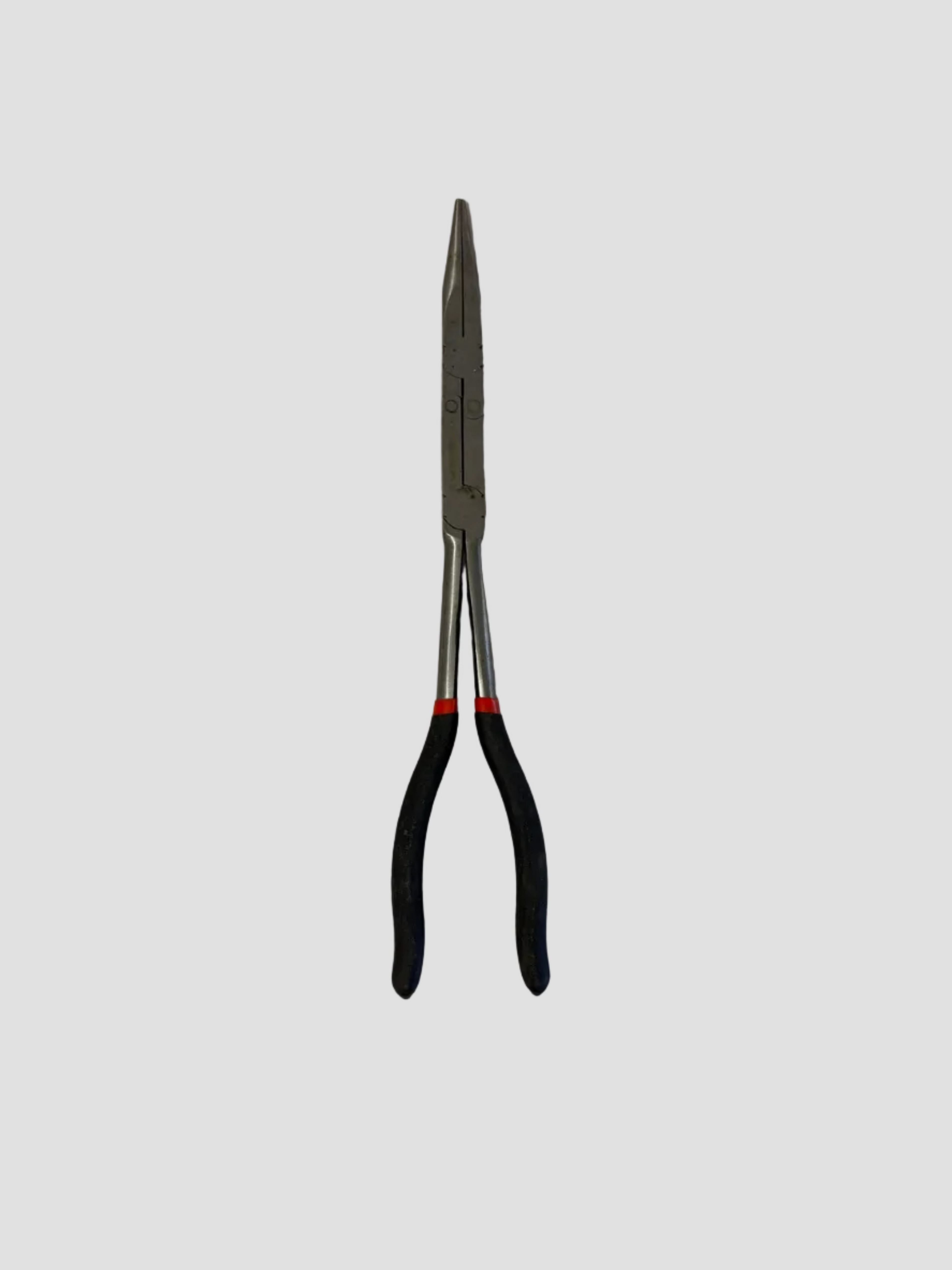 A pair of needle-nose pliers with silver metal jaws and black handles with a red accent ring, lying on a light gray surface.