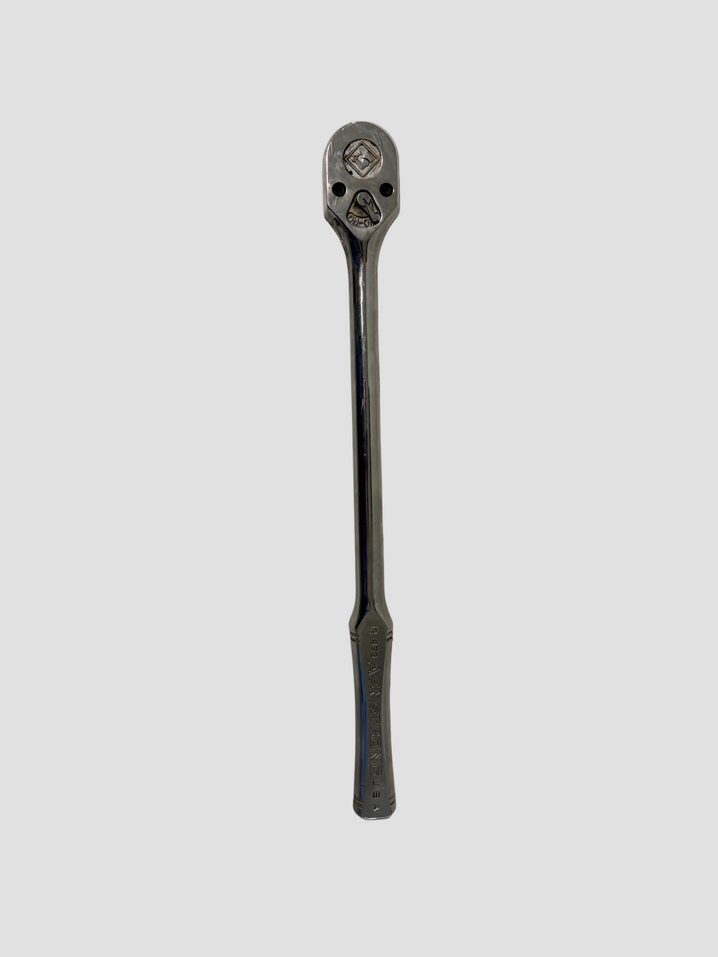 A chrome Armstrong ratchet wrench lying flat on a light-colored surface. The wrench has a long, polished handle engraved with “ARMSTRONG USA” and a rounded ratcheting head featuring a square drive socket connector and directional switch. The reflective metal surface highlights its durable, professional-grade construction.