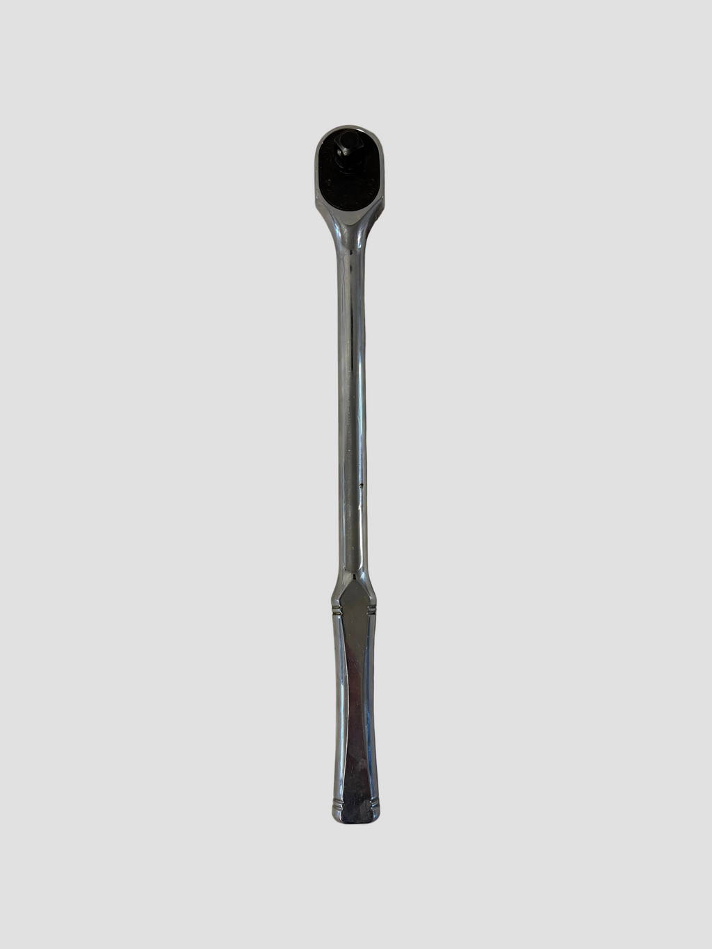 A chrome ratchet wrench lying flat on a light-colored surface. The wrench has a polished metallic finish with a long, slightly curved handle and a rounded ratcheting head featuring a square drive socket connector and directional switch. The reflective surface highlights its smooth contours and durable construction.