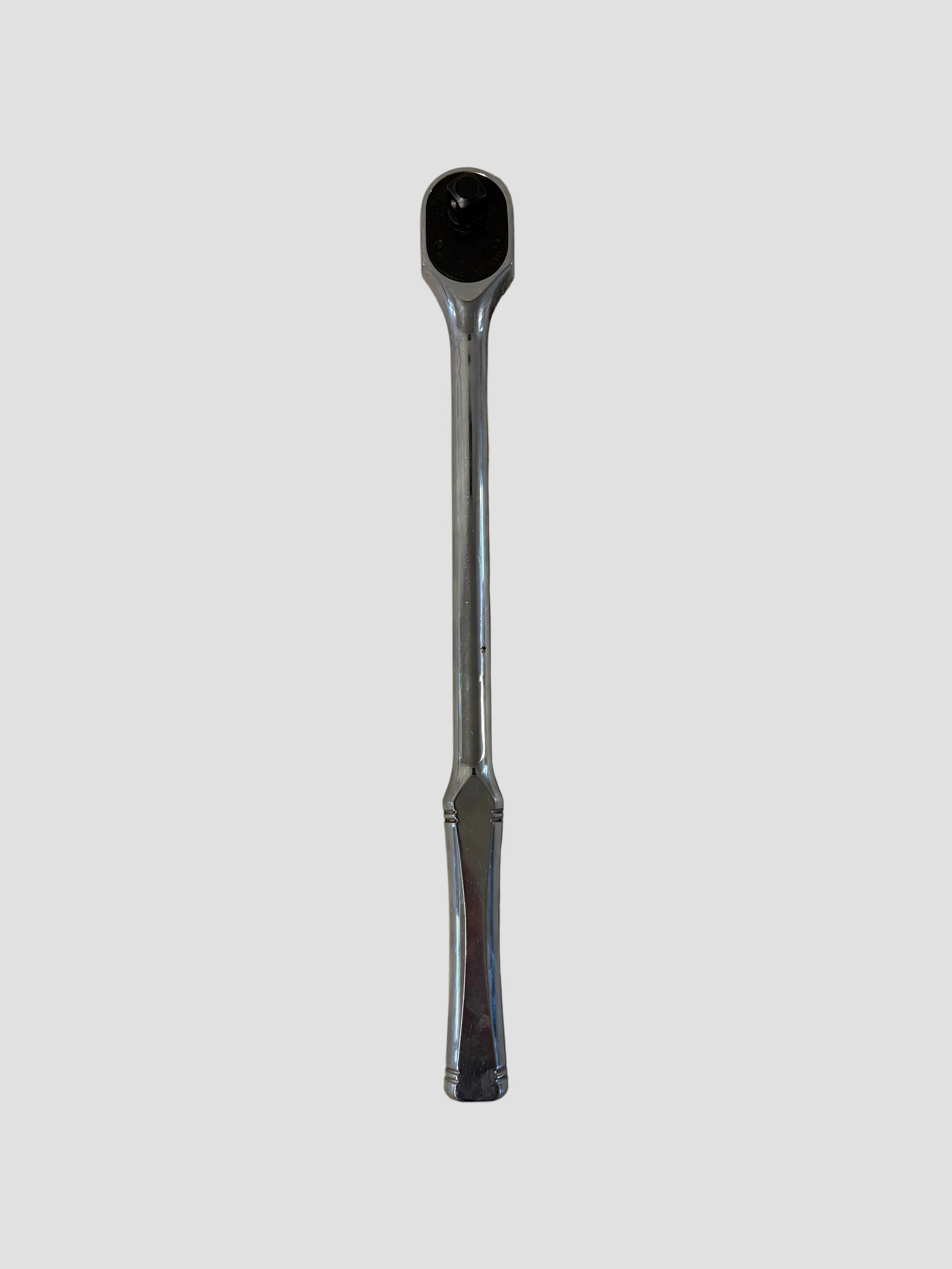 A chrome ratchet wrench lying flat on a light-colored surface. The wrench has a polished metallic finish with a long, slightly curved handle and a rounded ratcheting head featuring a square drive socket connector and directional switch. The reflective surface highlights its smooth contours and durable construction.