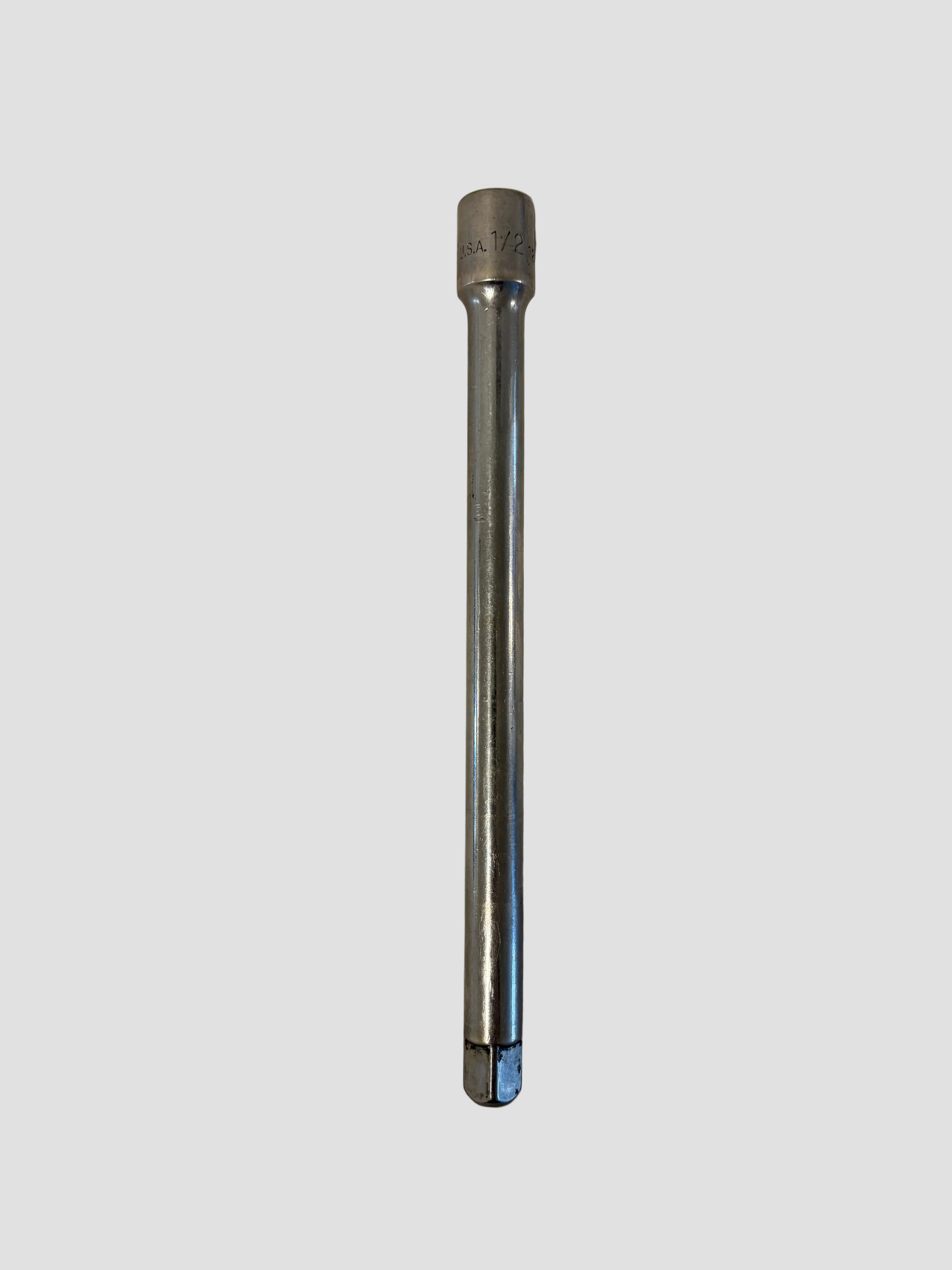 A chrome hex socket tool bit with a 1/4 inch shank, shown vertically on a light beige surface.