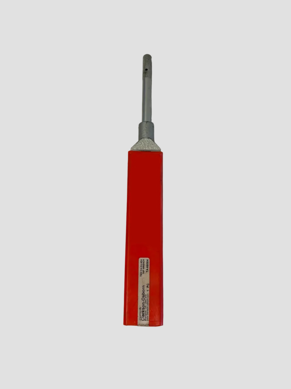 A red and silver metal tool, possibly a specialized screwdriver or hand tool, with handwritten black ink on the red handle, lying on a light gray surface.