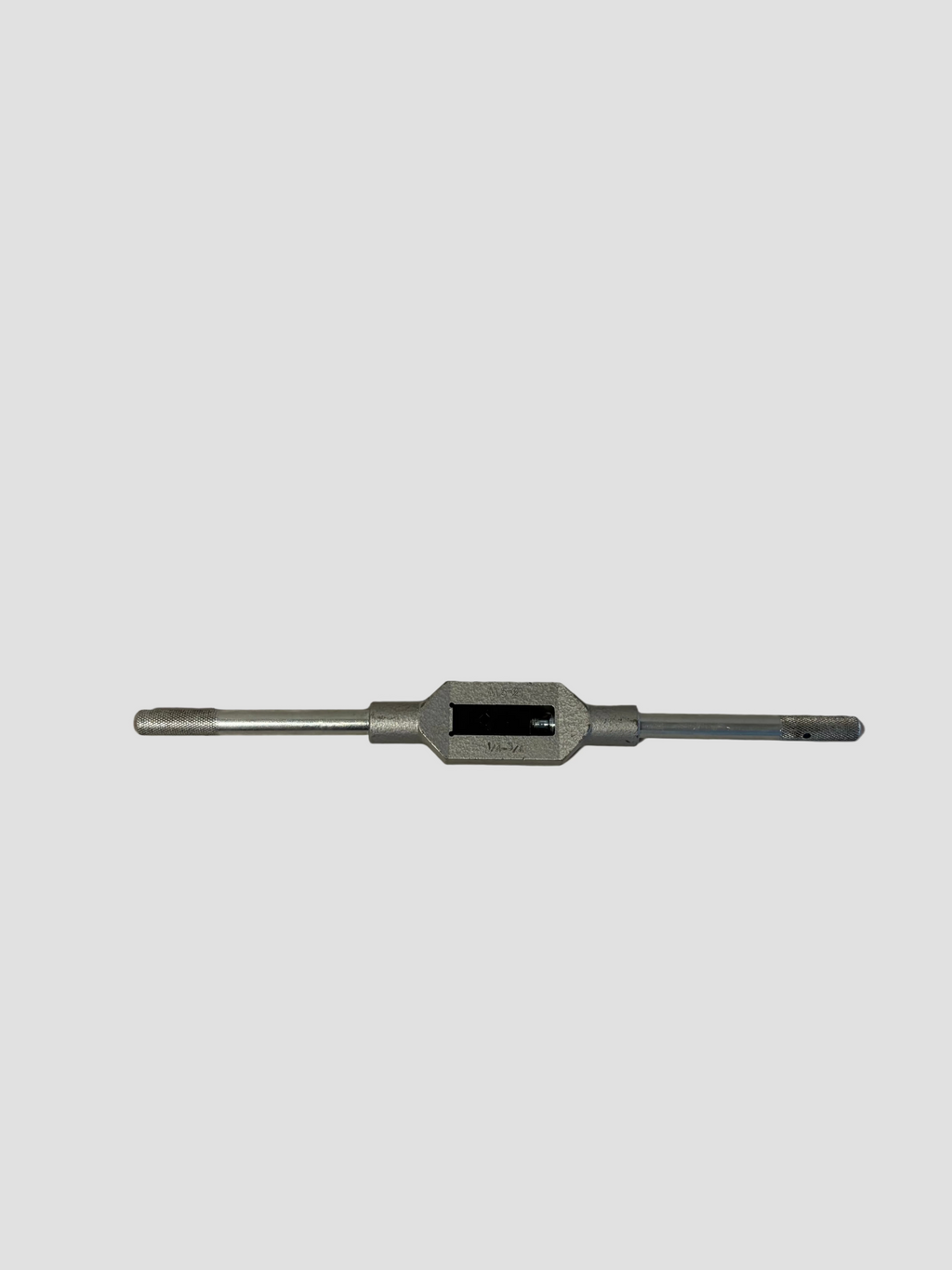 A silver metal pipe thread die or tap tool lying horizontally on a plain off-white surface.