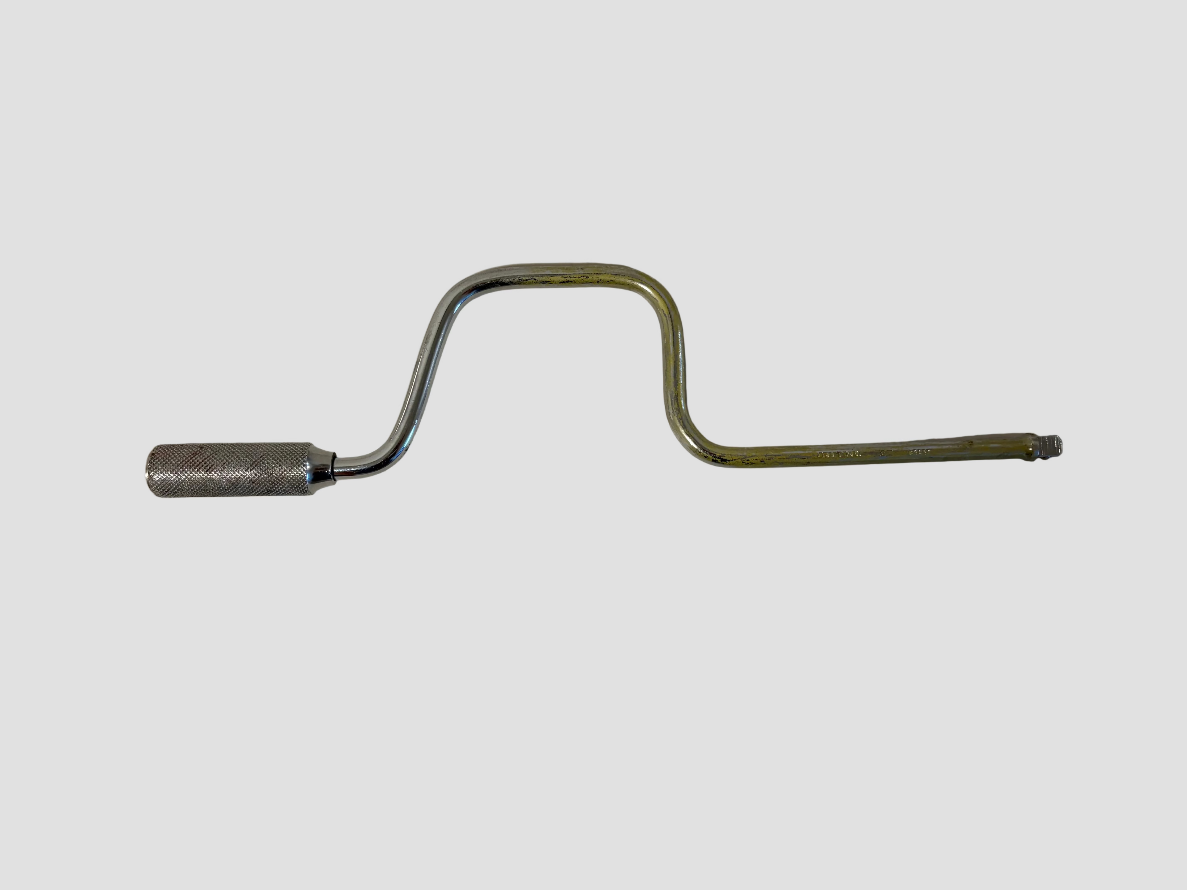 A bent metal tool with a silver cylindrical end and a yellowed, worn shaft, photographed on a plain off-white surface.