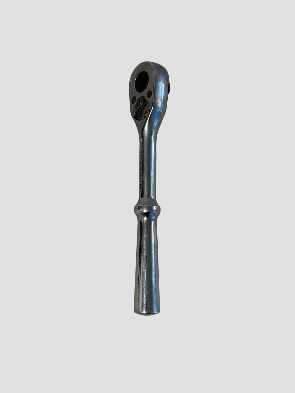 A chrome ratchet wrench with a straight handle, photographed vertically against a plain, slightly textured off-white background.