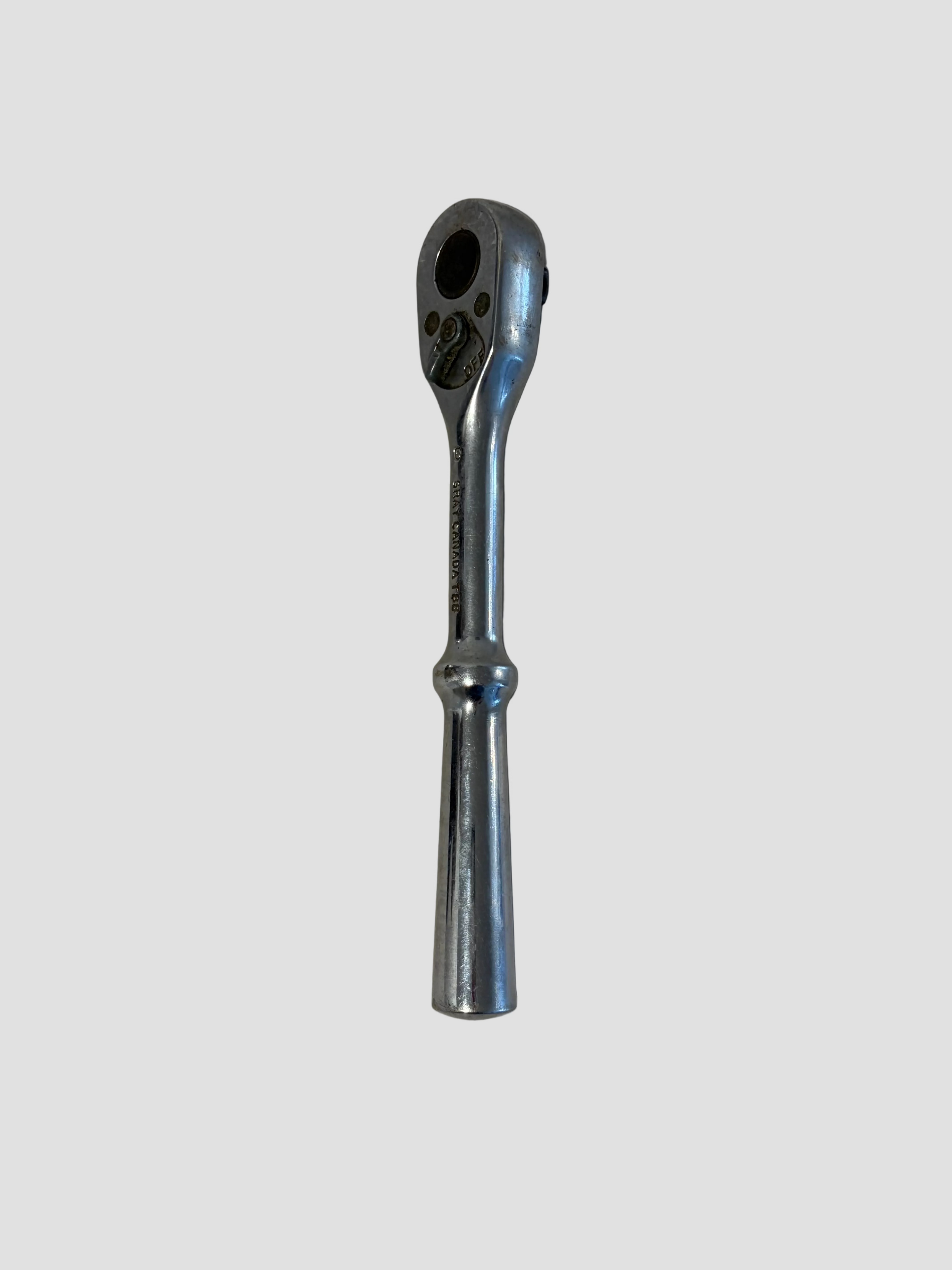 A chrome ratchet wrench with a straight handle, photographed vertically against a plain, slightly textured off-white background.
