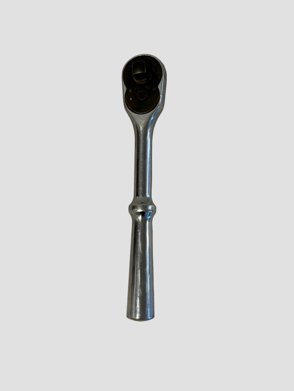 A chrome ratchet wrench with a black socket head, shown vertically on a light beige textured surface.