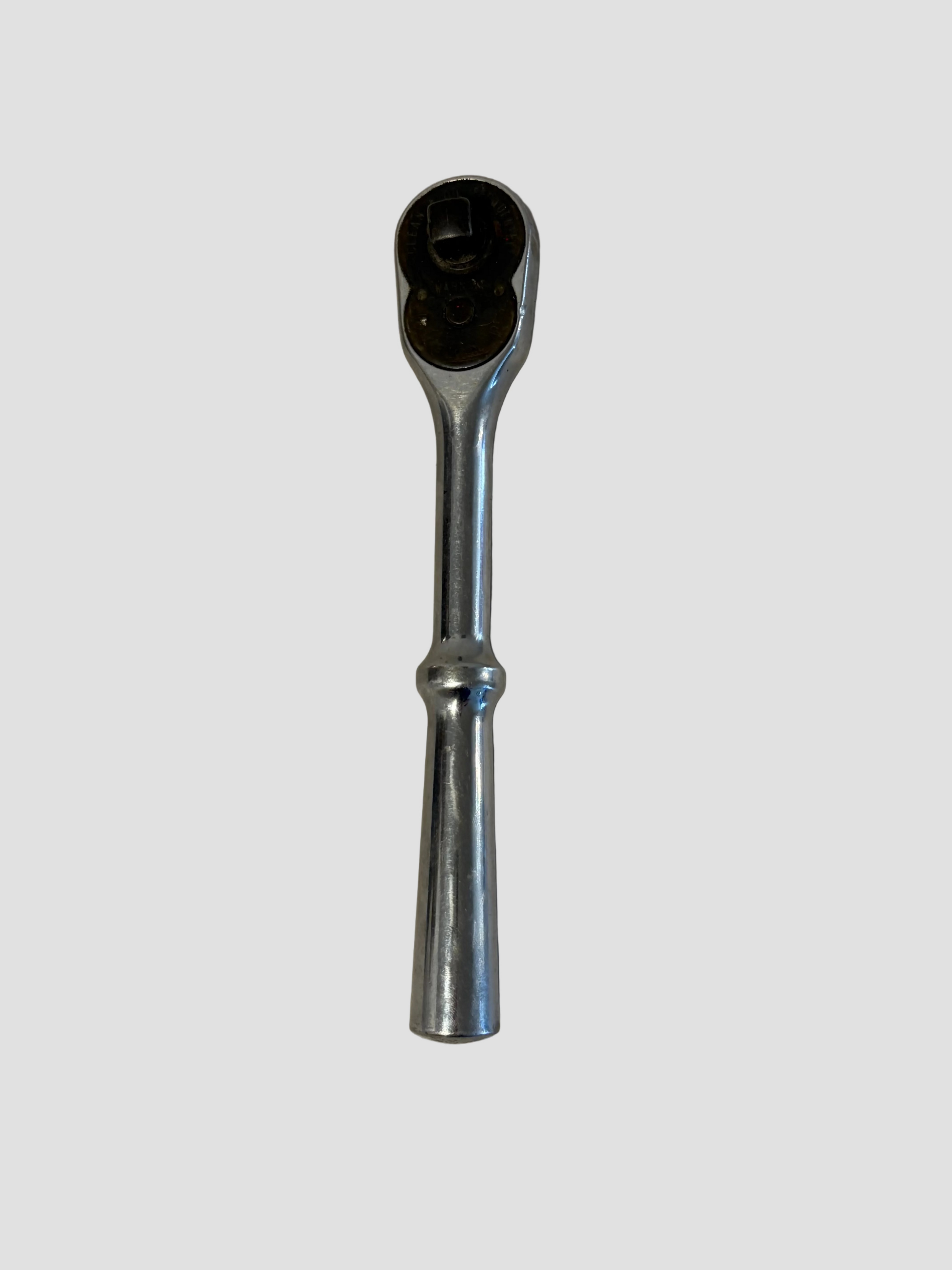 A chrome ratchet wrench with a black socket head, shown vertically on a light beige textured surface.