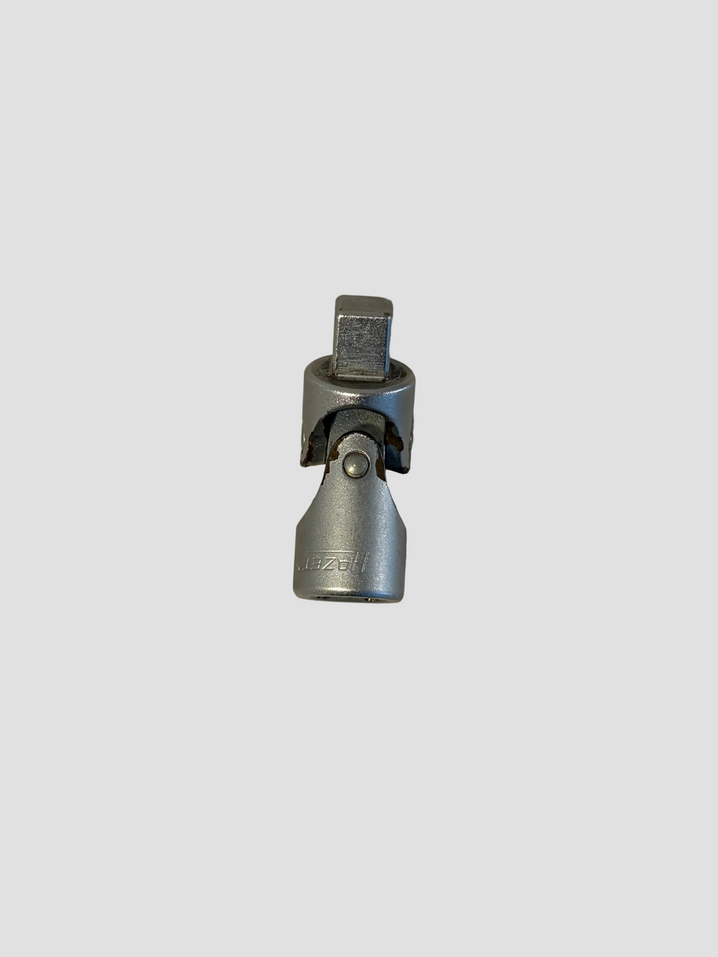 A small silver metal hardware component, possibly a connector or clamp, photographed on a plain off-white surface.