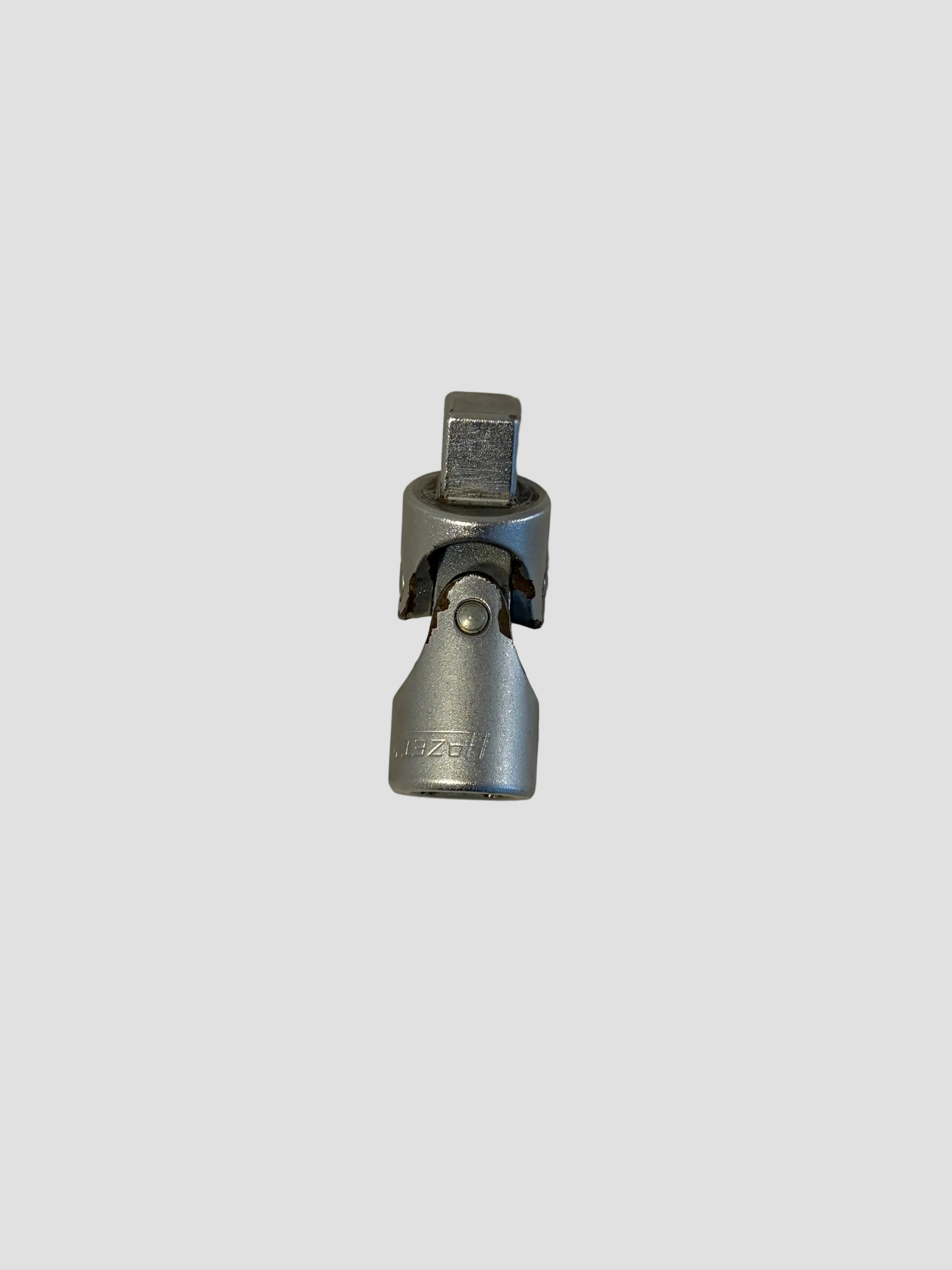 A small silver metal hardware component, possibly a connector or clamp, photographed on a plain off-white surface.
