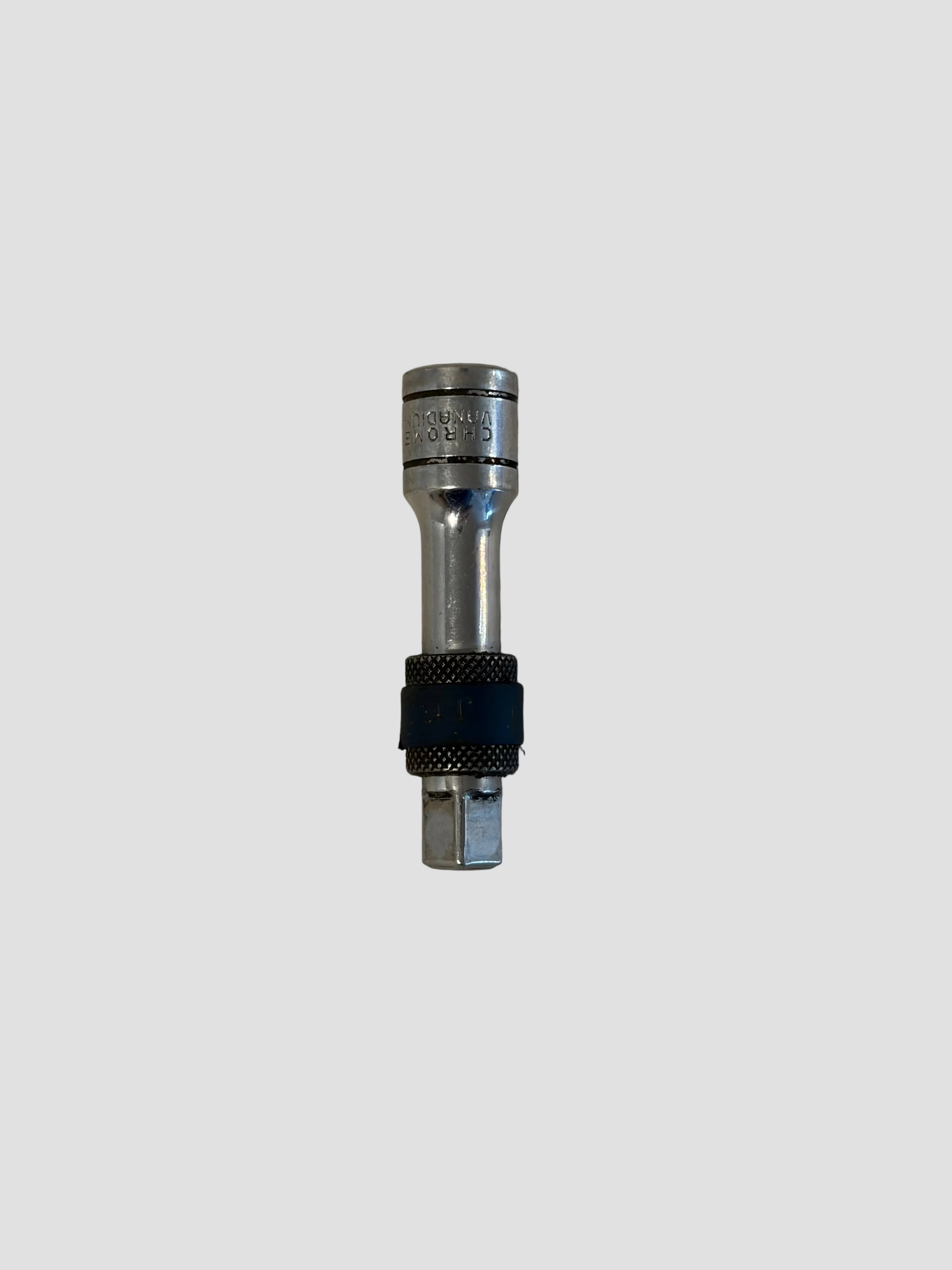 A silver metal socket tool adapter with a black textured grip band, photographed on a light beige surface.