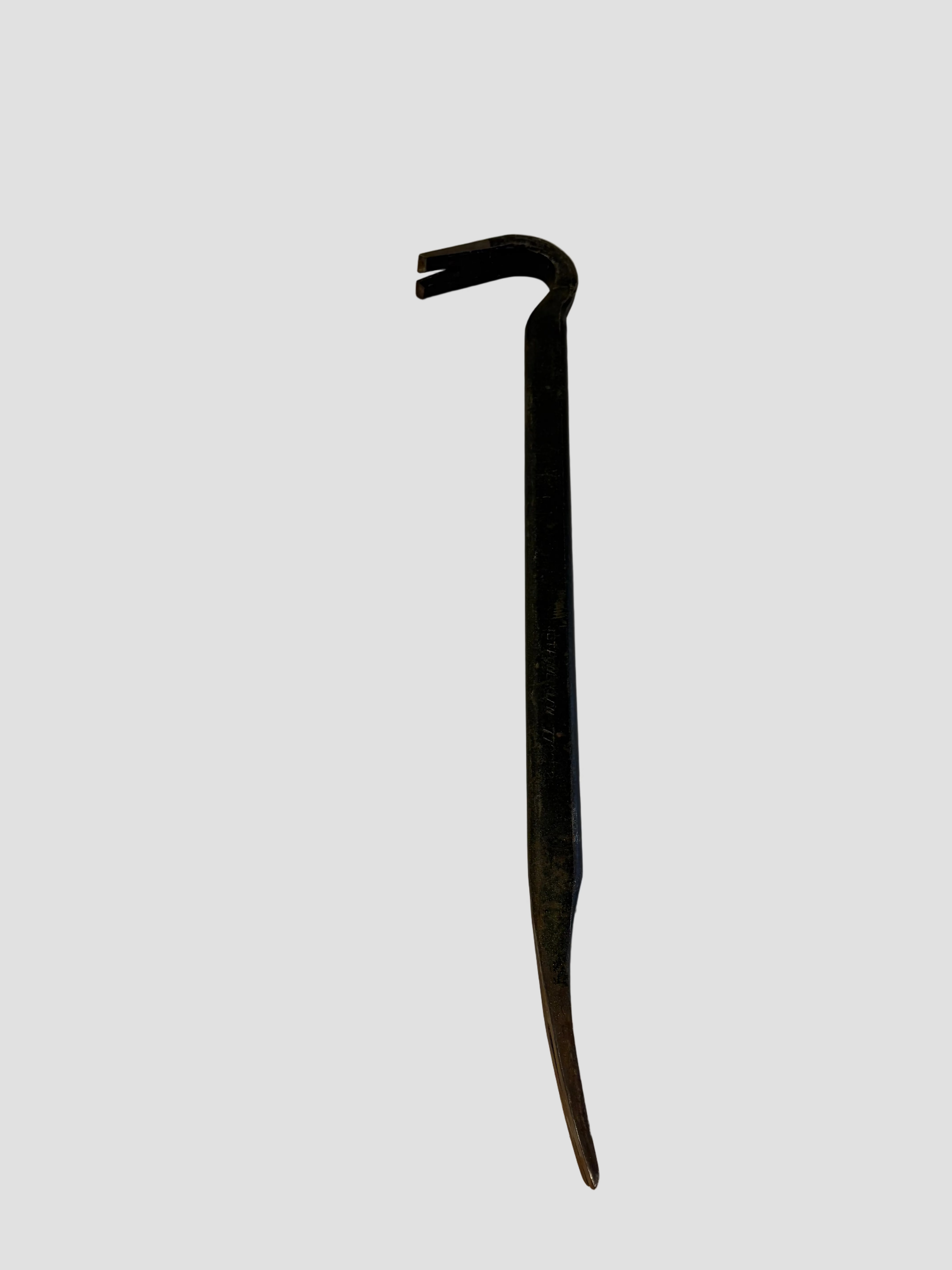 A metal crowbar resting on a light-colored surface with a tiled floor visible below. The crowbar has a dark, worn finish and features a curved claw at one end for prying and a straight, tapered point at the other for leverage. Its sturdy steel construction and simple design make it ideal for demolition or nail removal tasks.